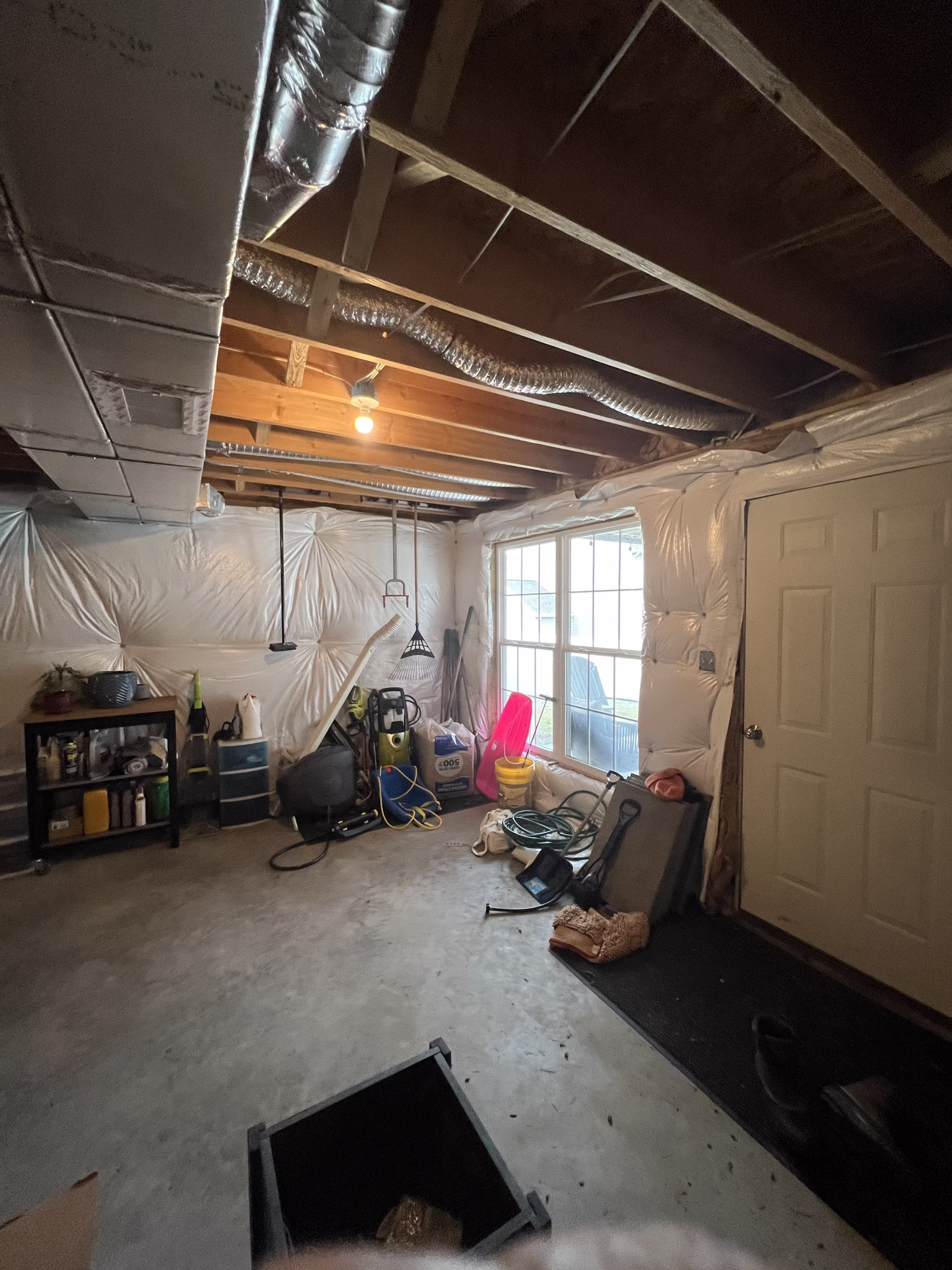 A cluttered basement storage space in Mechanicsburg, PA with tools, cleaning supplies, and a large window.