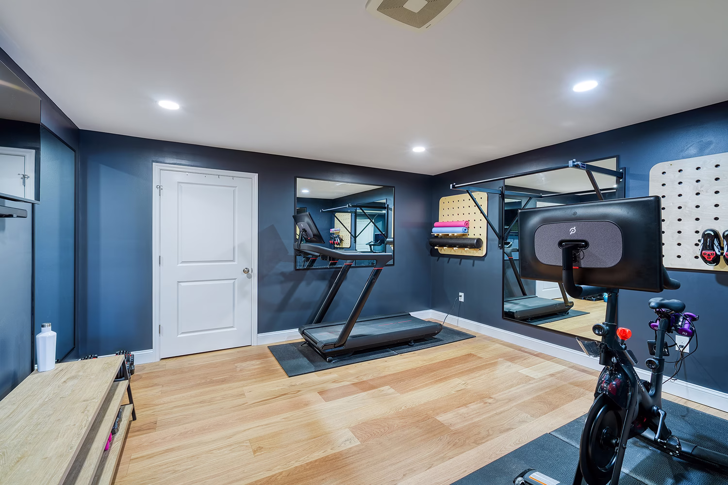 Modern home gym with treadmill and exercise bike in Mechanicsburg, PA. Features dark blue walls and wooden flooring.