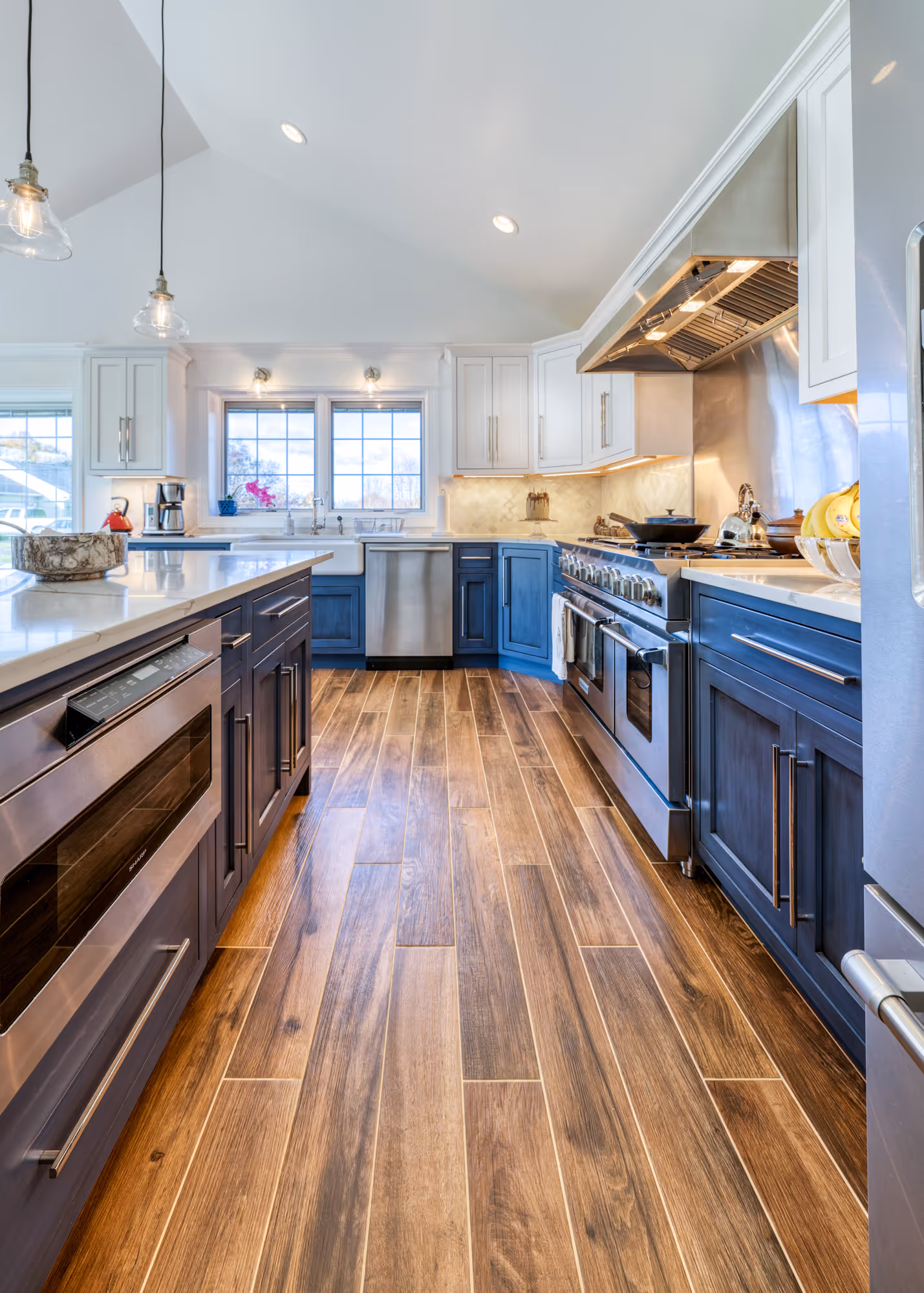 Modern kitchen in Etters, PA featuring blue and white cabinetry, stainless steel appliances, and wood tile flooring.