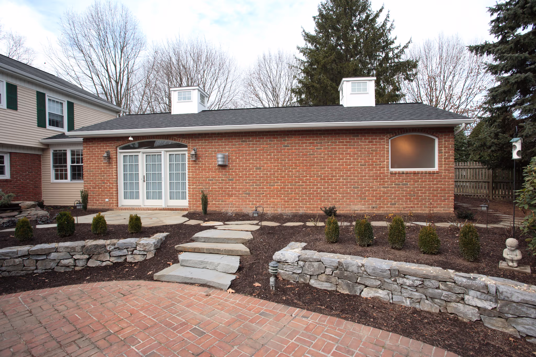A charming brick exterior of a modern garden room in Camp Hill, PA, featuring double doors and landscaped stone details.