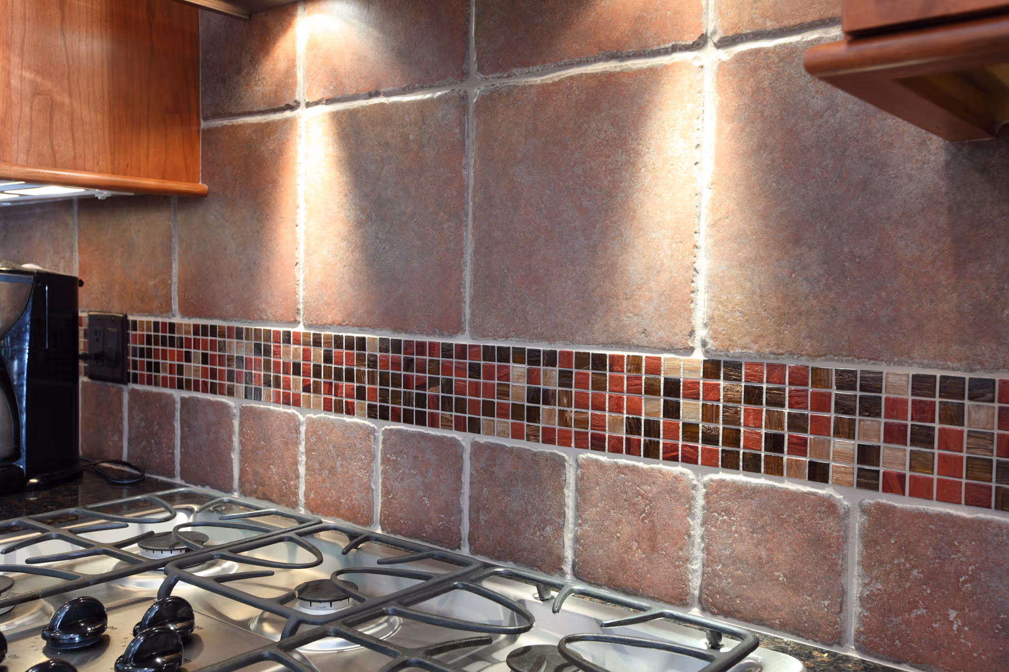 Rustic kitchen backsplash with textured red and brown tiles, showcasing a gas stove in Carlisle, PA.