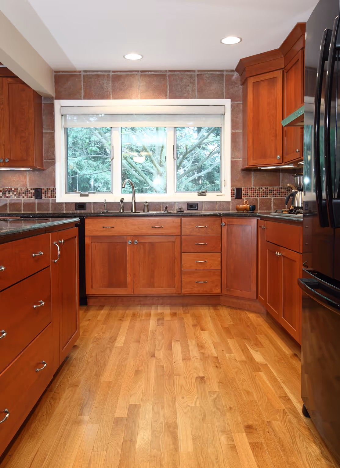 Modern kitchen in Carlisle, PA featuring rich wood cabinets, granite countertops, and large window overlooking greenery.