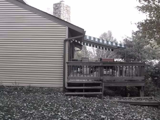 Exterior view of a house in Carlisle, PA featuring a wooden deck and stone chimney under a striped awning.