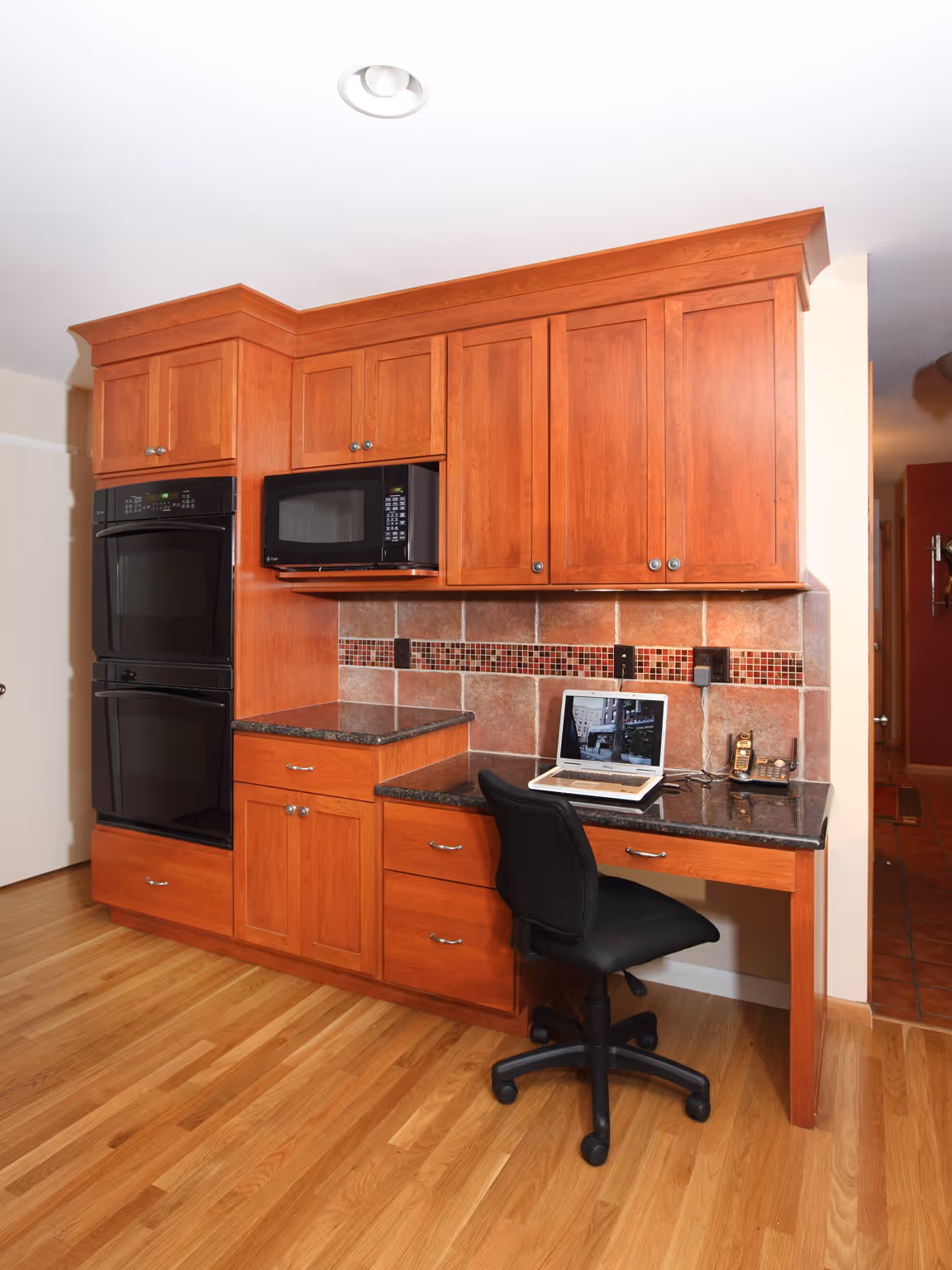 Modern kitchen in Carlisle, PA featuring cherry wood cabinetry, granite countertops, and a workspace with a laptop.