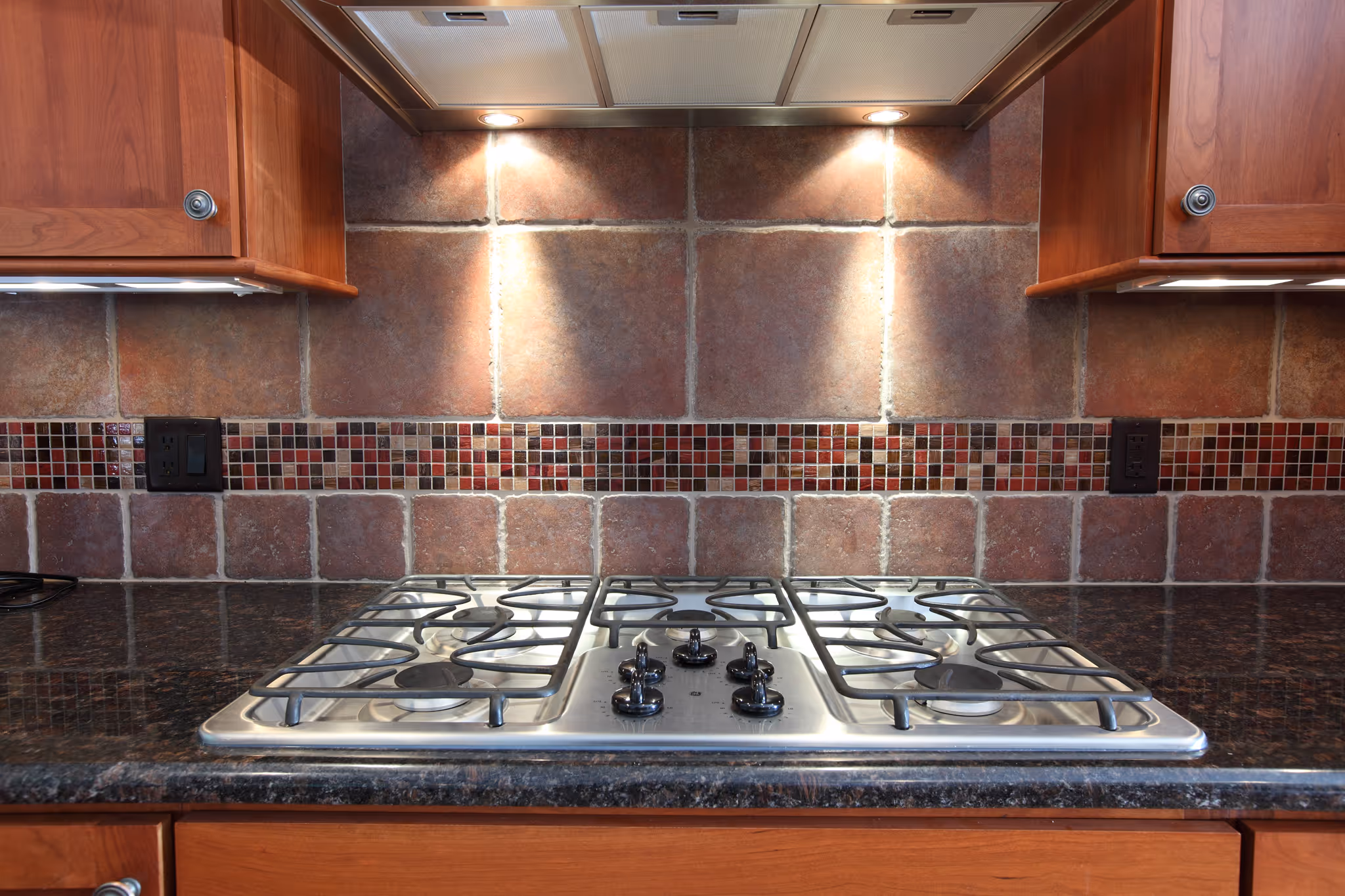 Modern kitchen in Carlisle, PA featuring a black granite countertop, stainless steel gas range, and mosaic tile backsplash