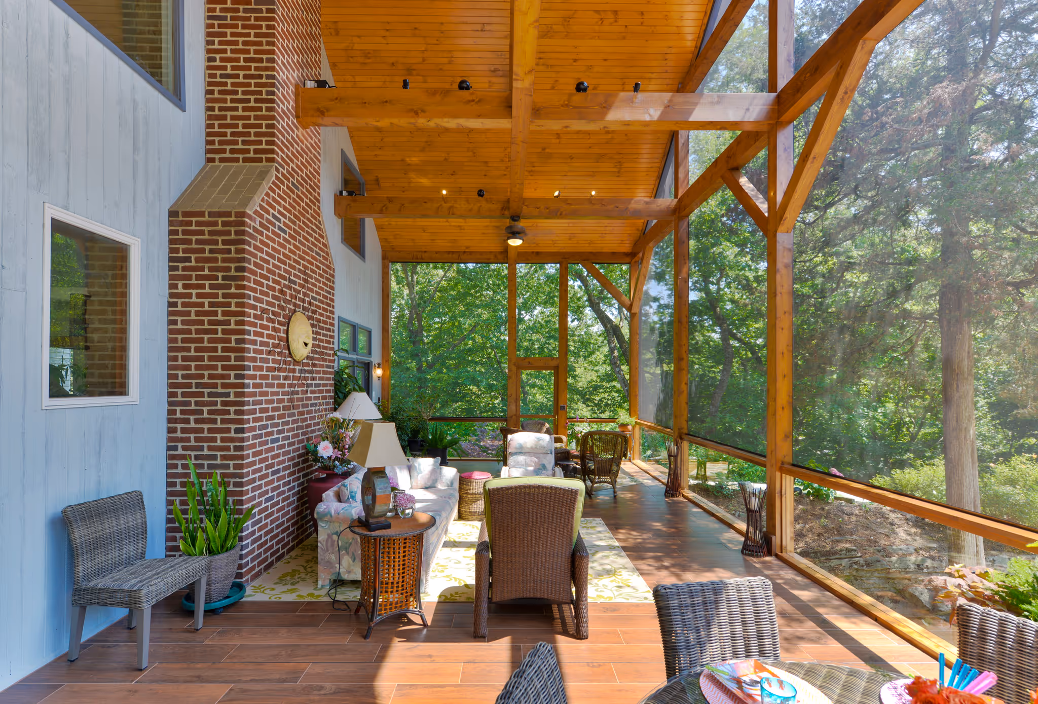 Cozy screened-in porch with wooden ceiling and brick accent, filled with floral-patterned furniture and greenery in camp hill, pa.