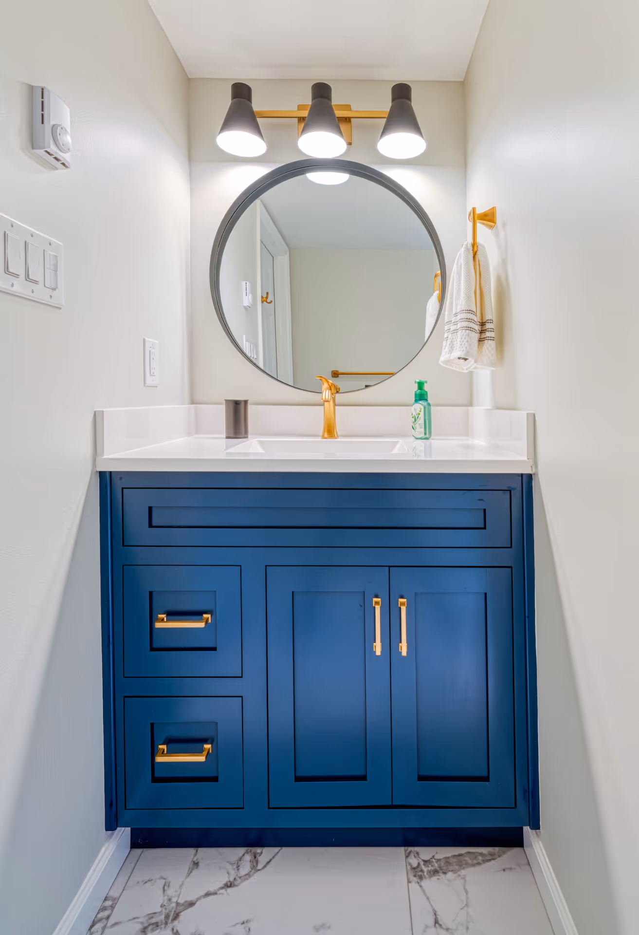 Stylish blue bathroom vanity with gold accents and round mirror in a modern design located in new cumberland, pa.