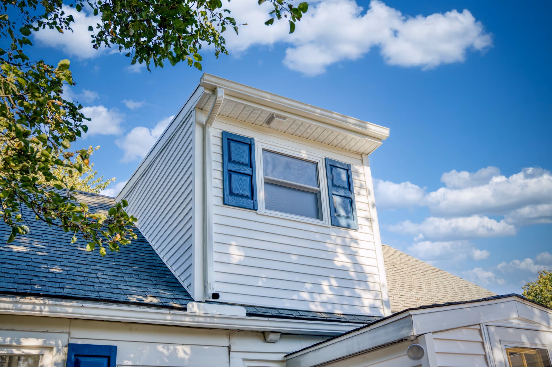 Transitional dormer with white siding and blue shutters in New Cumberland, PA under a clear blue sky