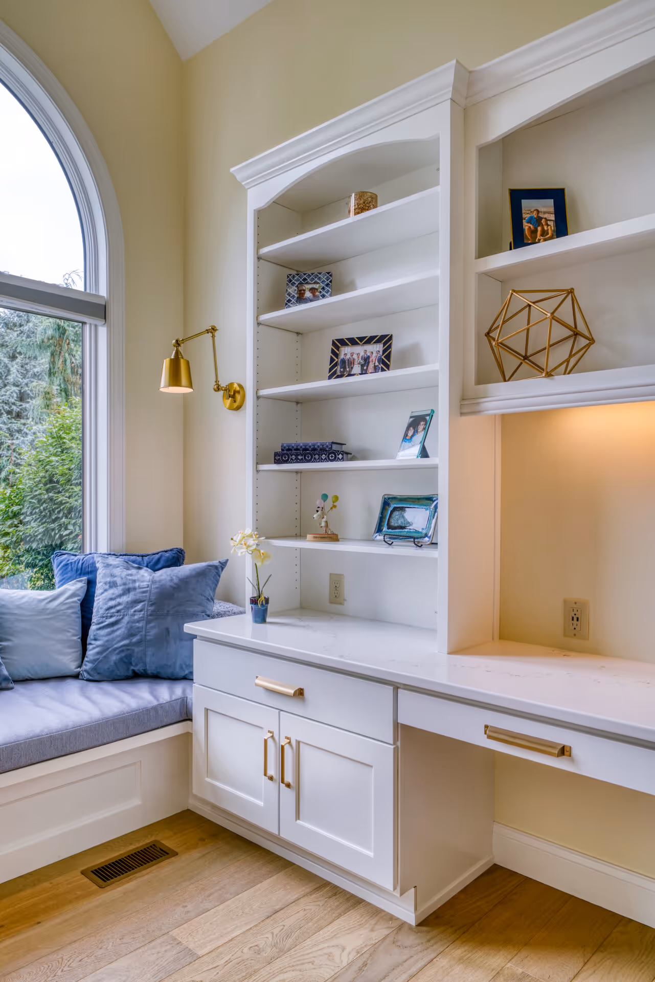 Modern home office in Mechanicsburg, PA featuring white cabinetry, a cozy reading nook with blue pillows, and stylish decor.