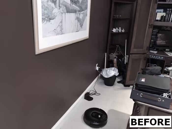 Home office with dark brown walls, cluttered desk space, robotic vacuum and framed artwork in Mechanicsburg, PA.