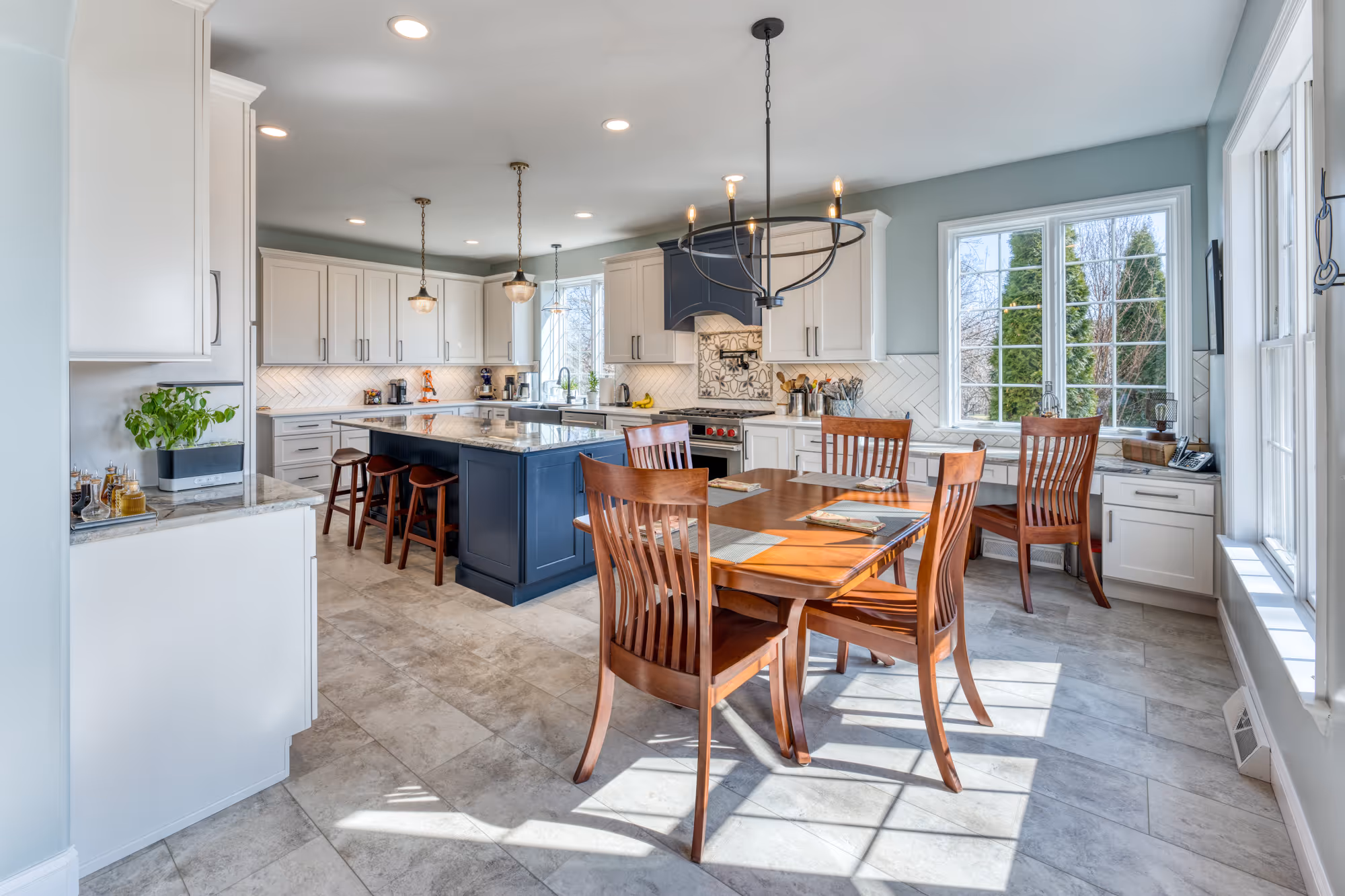 Contemporary kitchen in Enola, PA featuring a dark blue island, wooden dining table, and modern lighting.