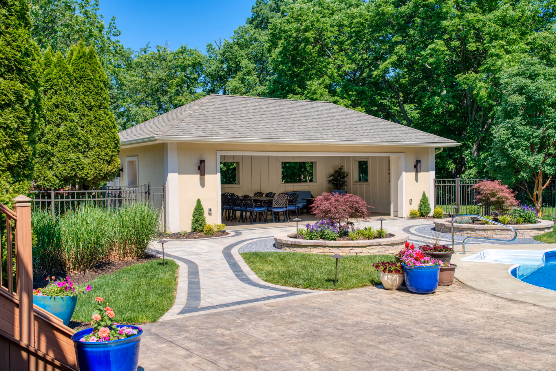 Modern poolhouse in Mechanicsburg, PA featuring outdoor dining area, lush greenery, and vibrant flowers.