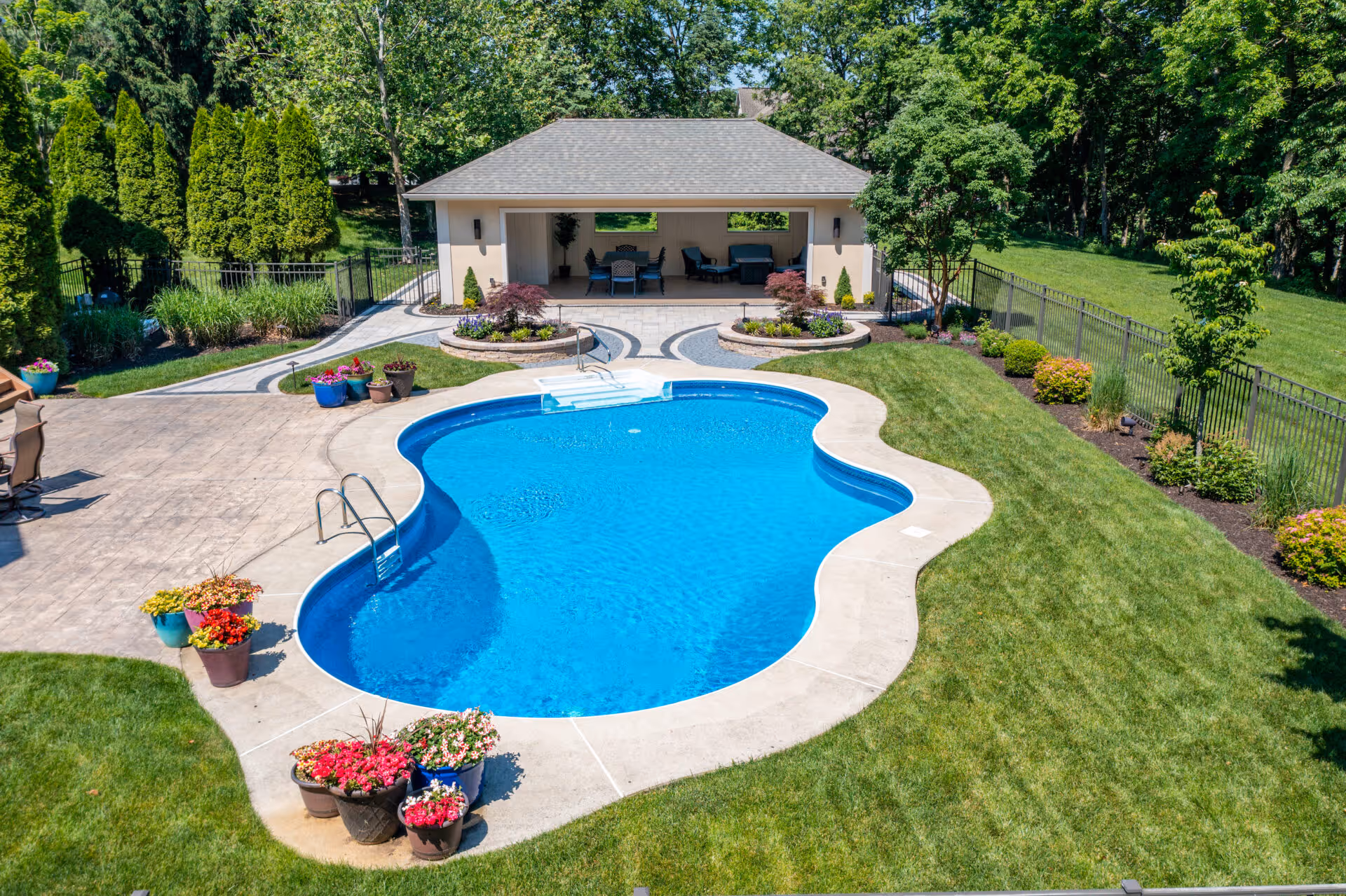 A beautiful outdoor pool area featuring a shaped blue pool, landscaped garden, and a shaded patio in Mechanicsburg, PA.
