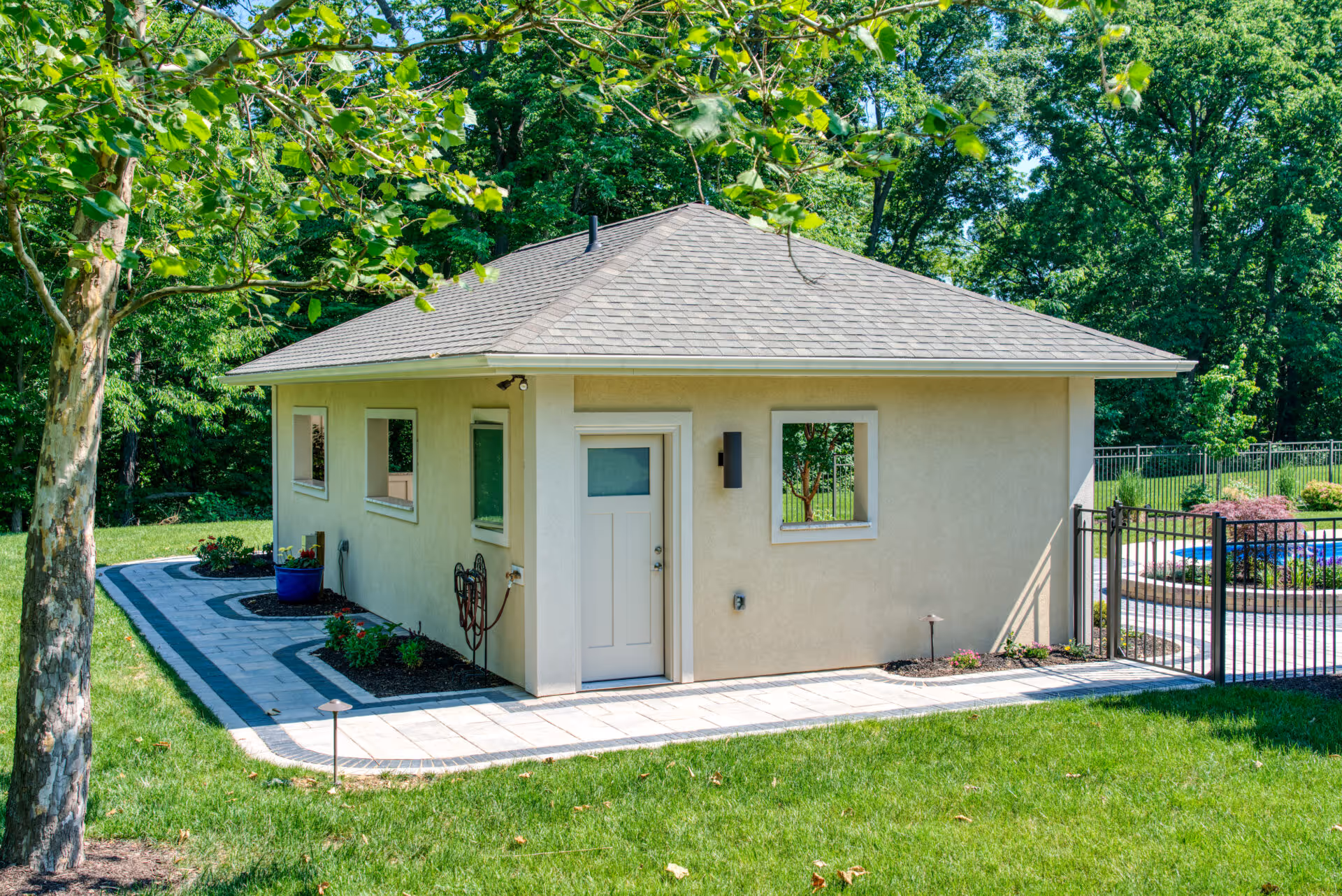 Modern poolhouse in Mechanicsburg, PA featuring a sleek design, surrounded by lush greenery and a paved pathway.