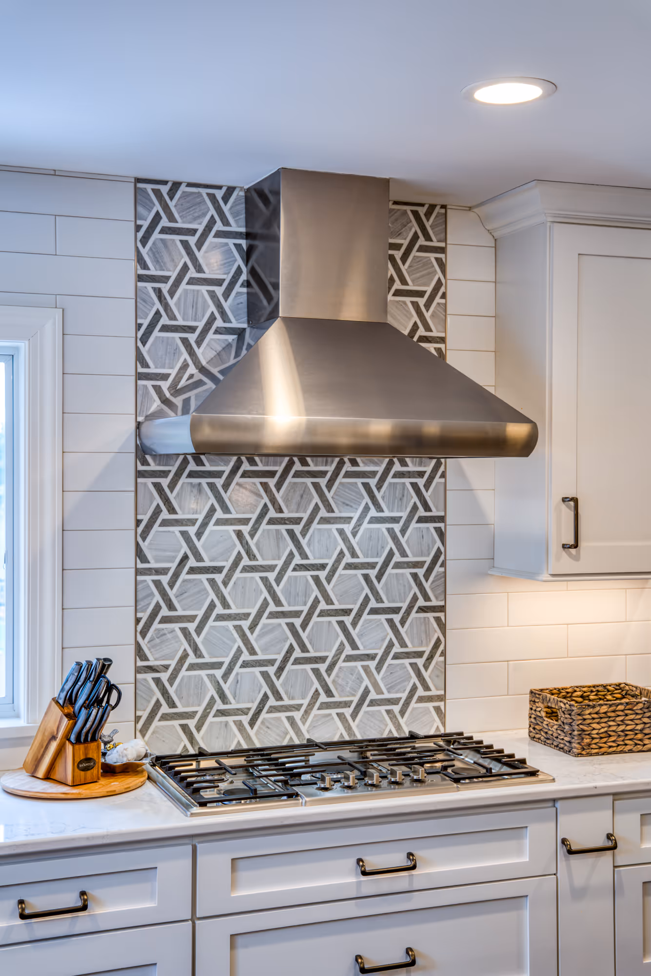 Modern kitchen in Marysville, PA featuring a geometric tile backsplash, stainless steel range hood, and white cabinetry.