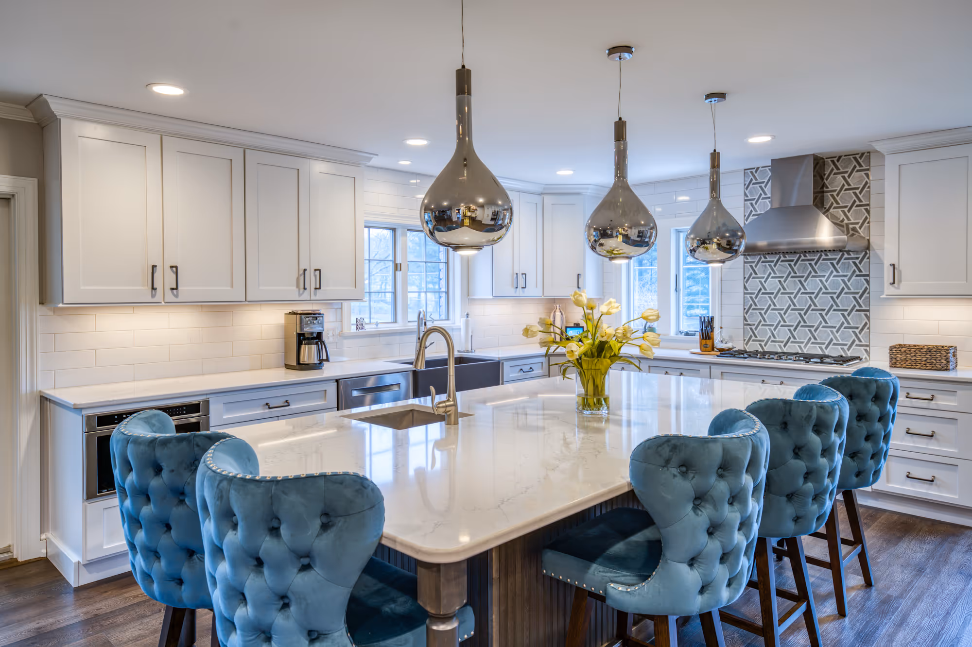 Modern kitchen in marysville, pa featuring sleek white cabinets, blue tufted bar stools, and metallic pendant lighting.