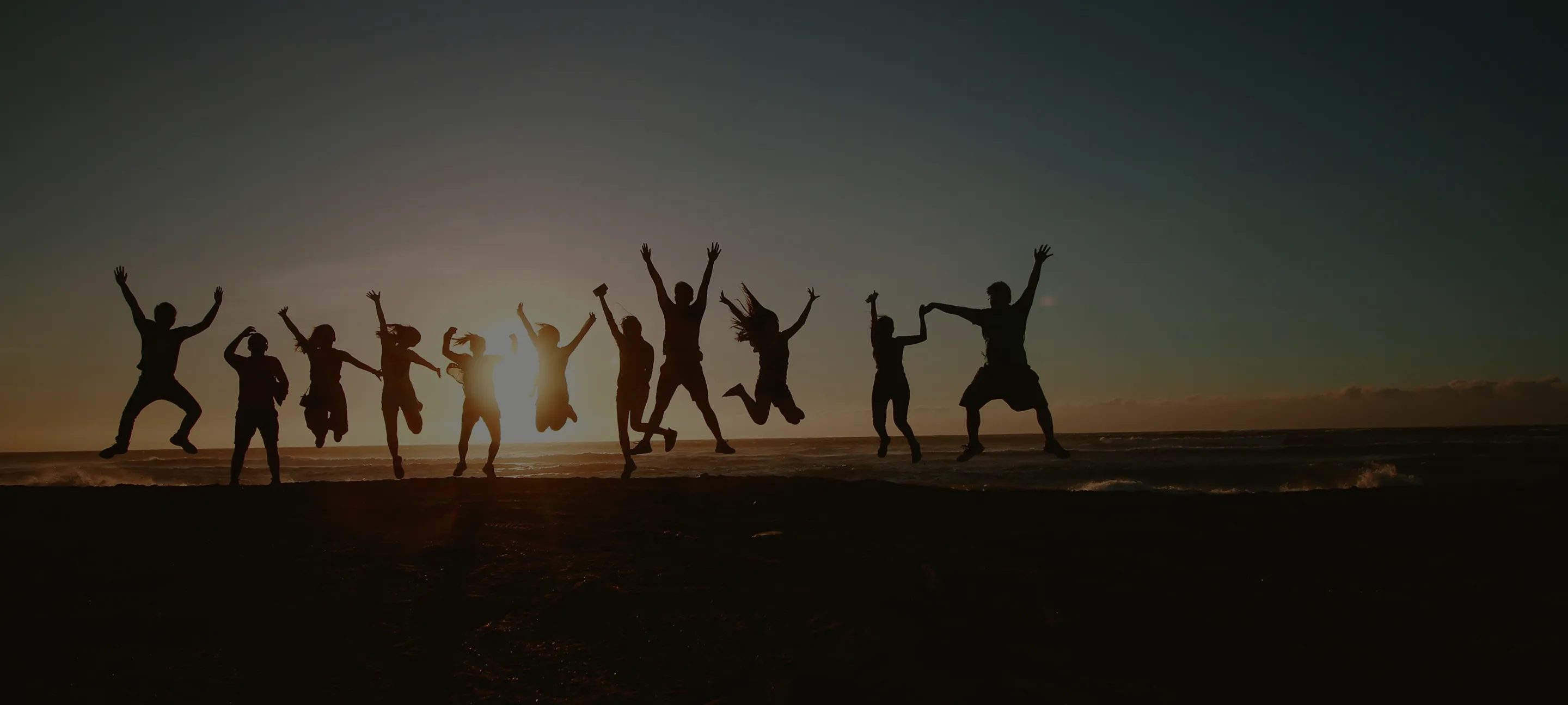 Silhouettes of a group of people jumping and celebrating on a beach at sunset.