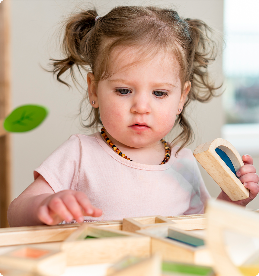 Young toddler with pigtails playing with wooden geometric blocks.
