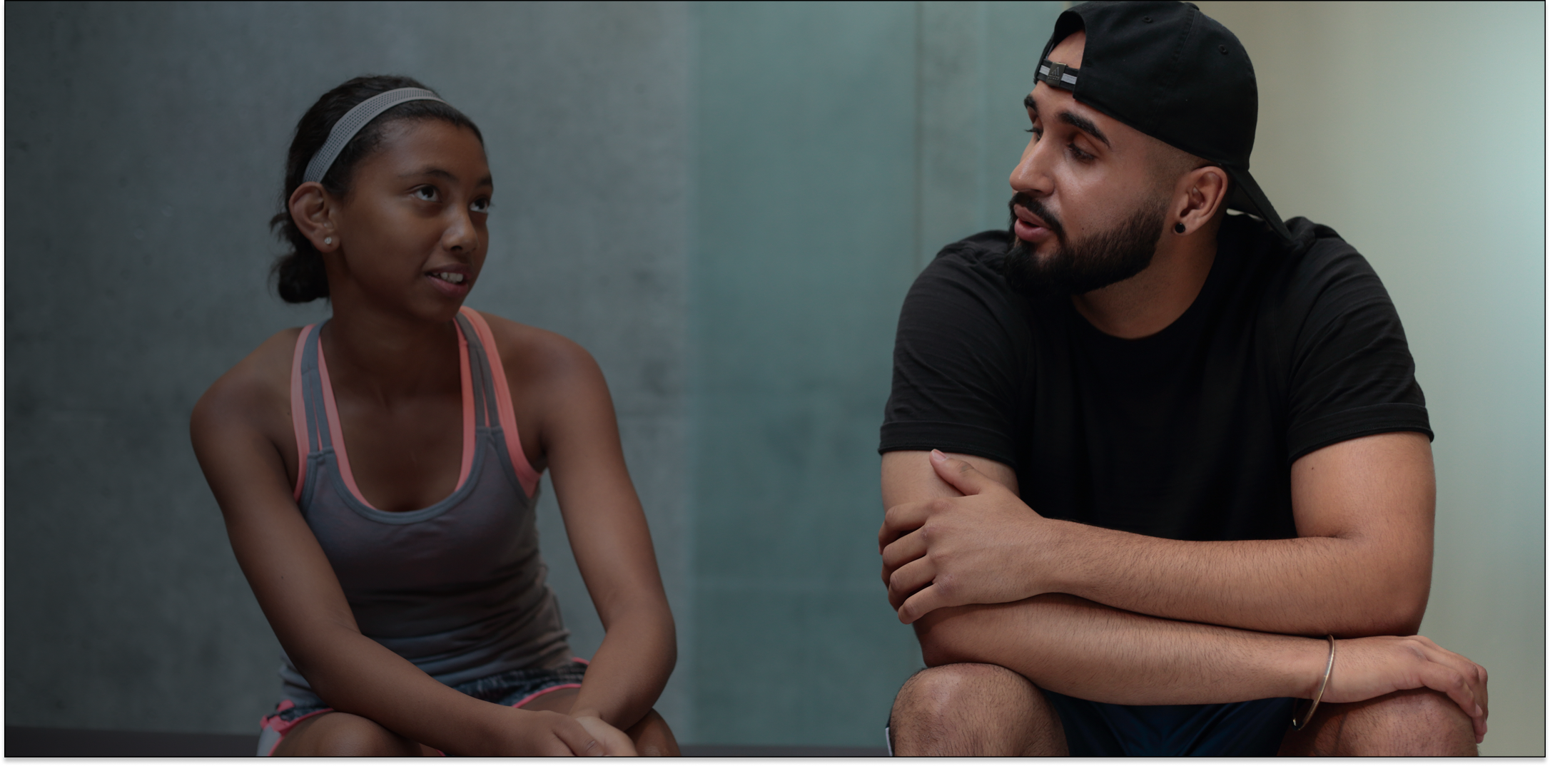 Athletic young woman and bearded man in casual sportswear sitting and talking indoors.