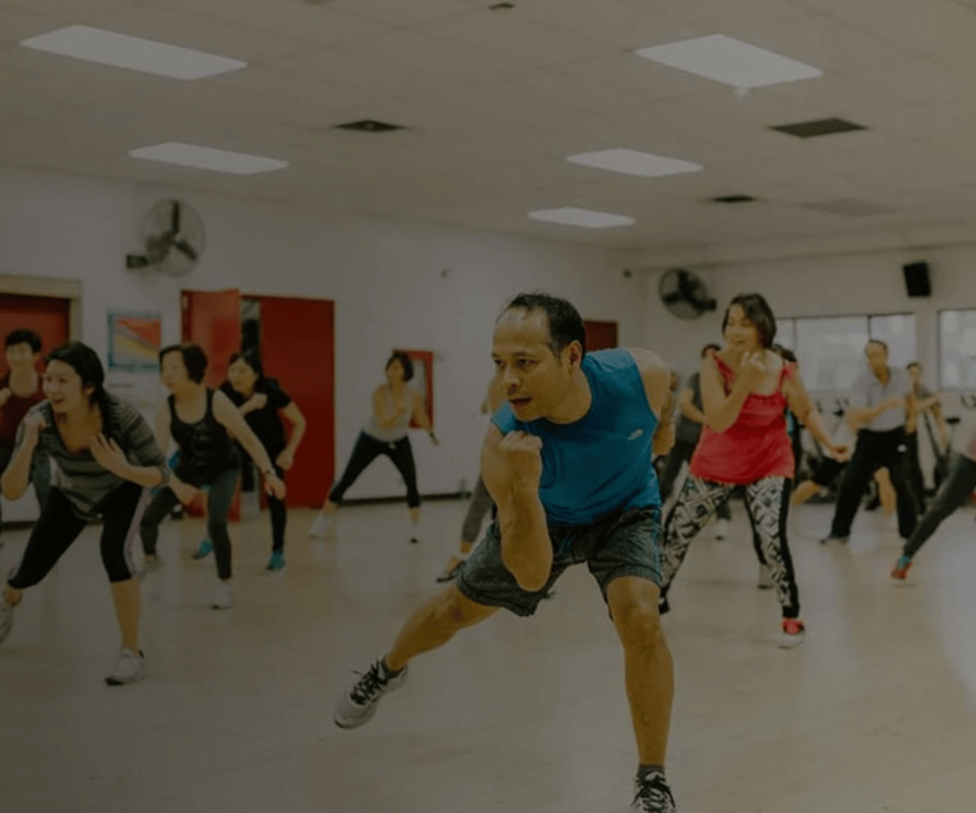 Group fitness class with participants in active workout poses led by an instructor in a blue shirt.