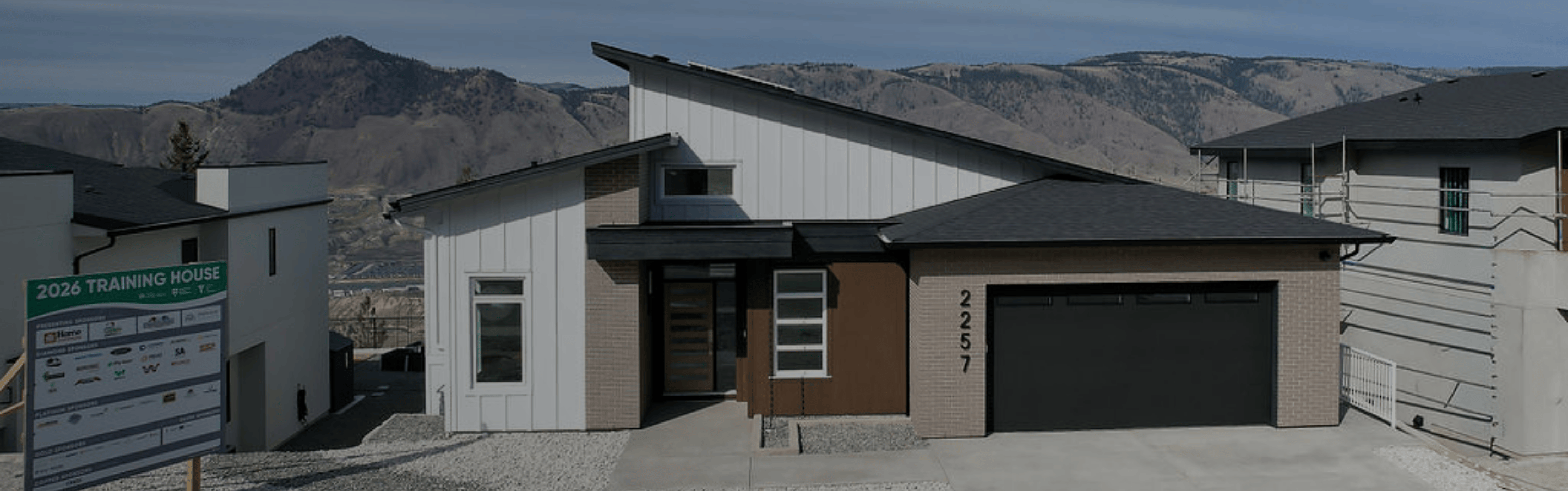 Large elegant house with multiple peaked roofs, three-car garage, and warm lit windows at dusk.