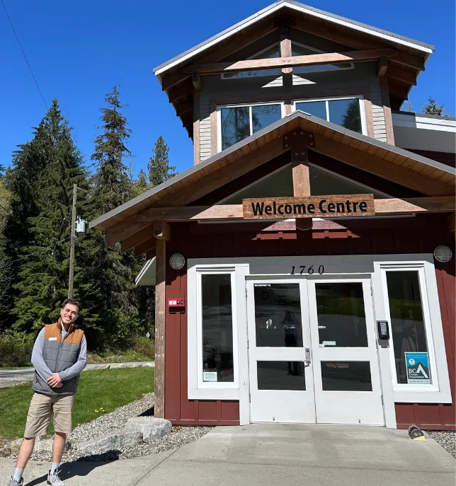 Man smiling outside a red Welcome Centre building with white doors and trees in the background.