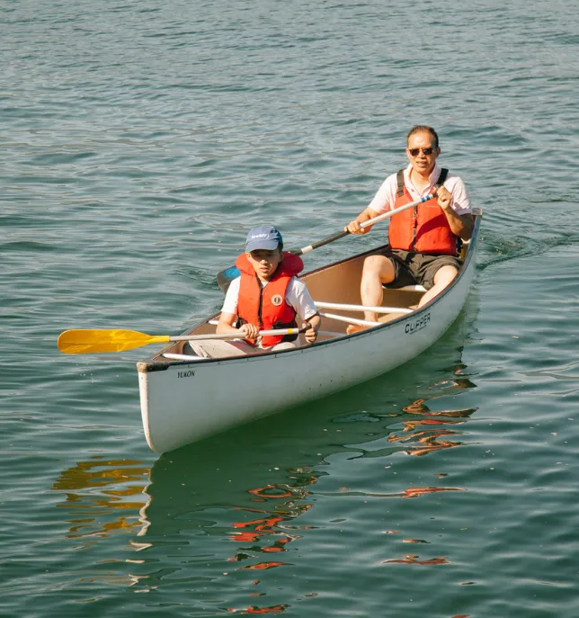 Two people wearing life jackets paddling a white canoe on calm water.