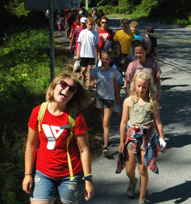 Group of children walking outside on a sunny day along a paved path surrounded by greenery.