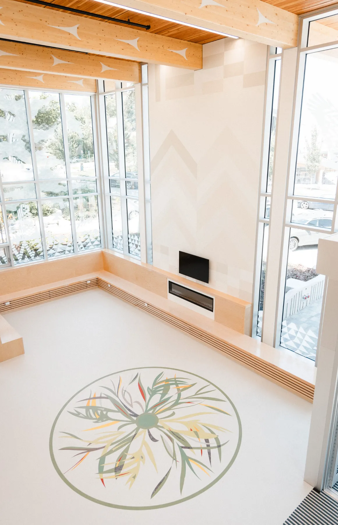 Spacious modern room with large windows, wooden ceiling beams, built-in bench, and a floral floor design.