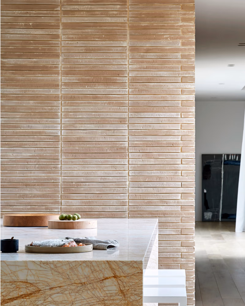 Modern kitchen with a beige stacked stone wall, a marble countertop island, wooden trays, and a folded gray cloth.