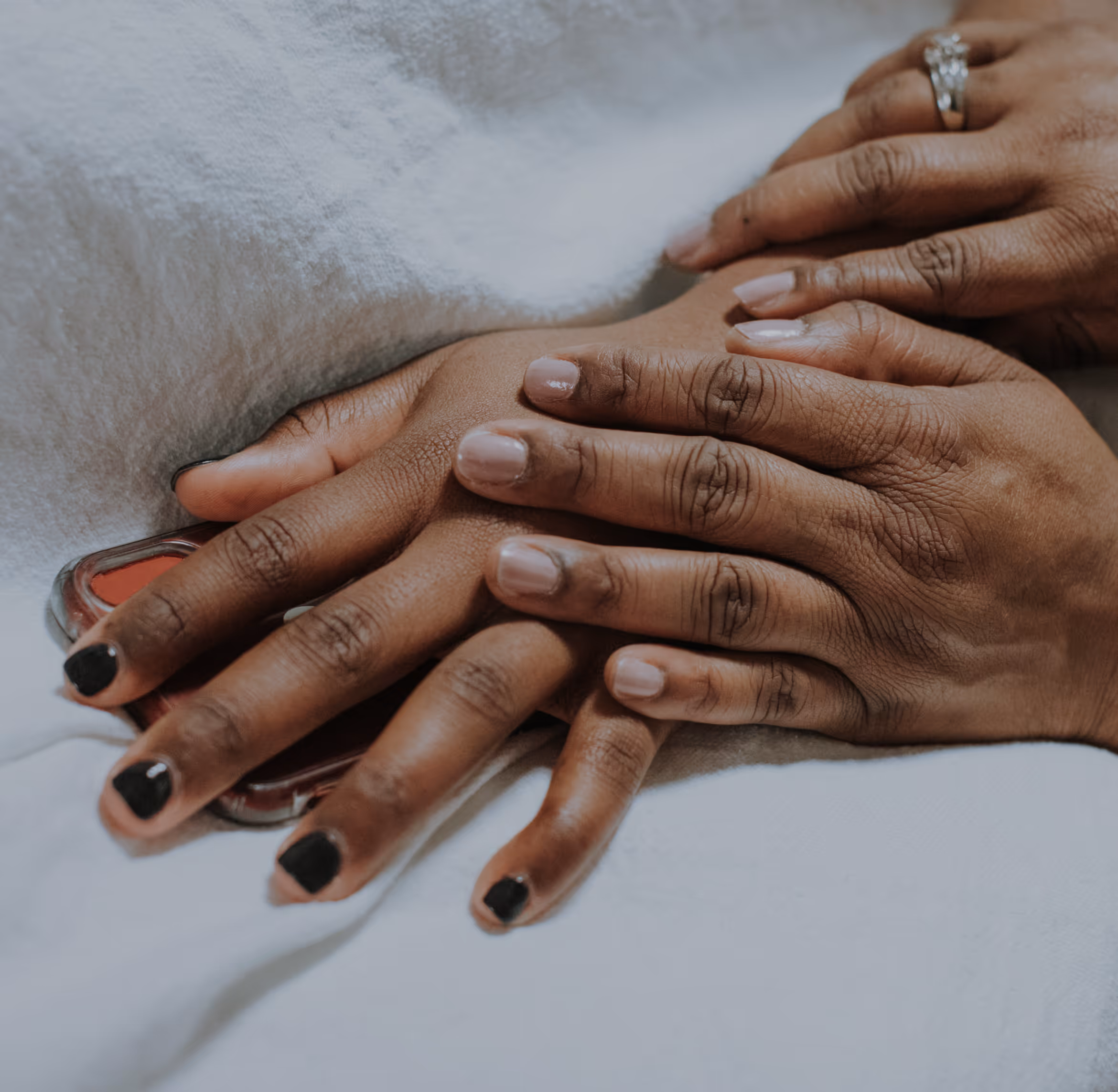 Close-up of two hands gently holding another hand, resting on a white surface
