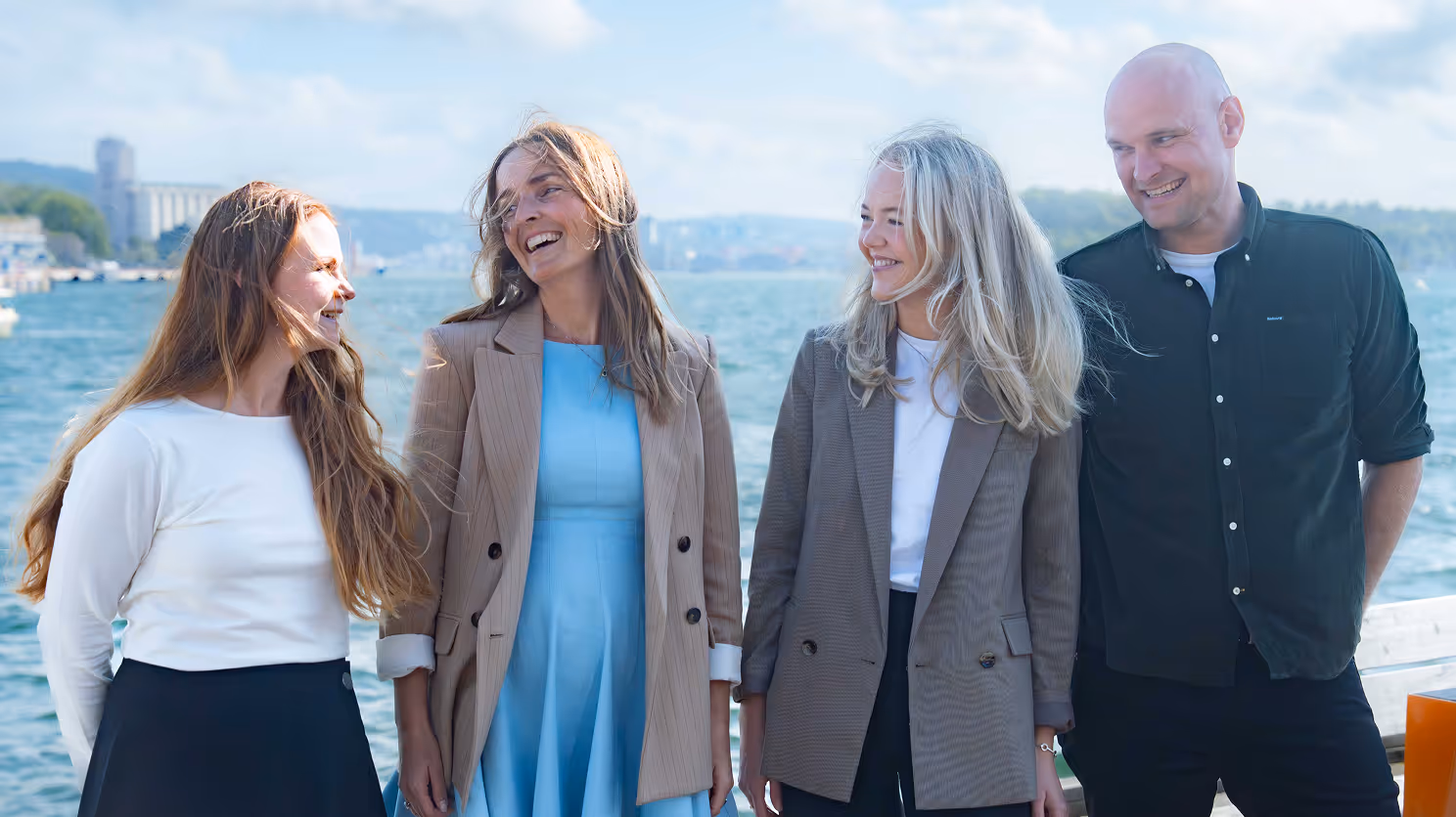 Four smiling adults standing by a waterfront under a partly cloudy sky.
