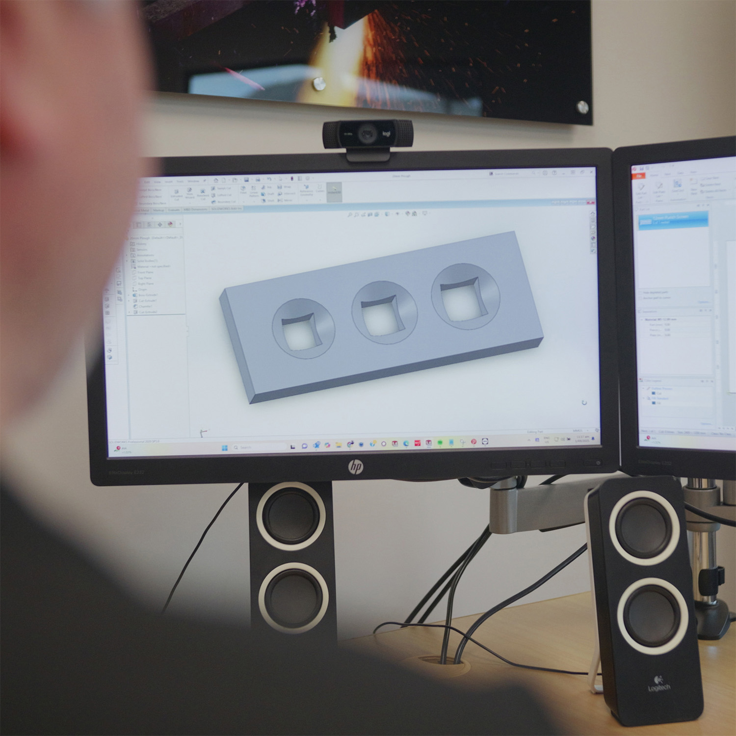 Person viewing a 3D CAD model of a rectangular block with three circular cutouts on a computer monitor.