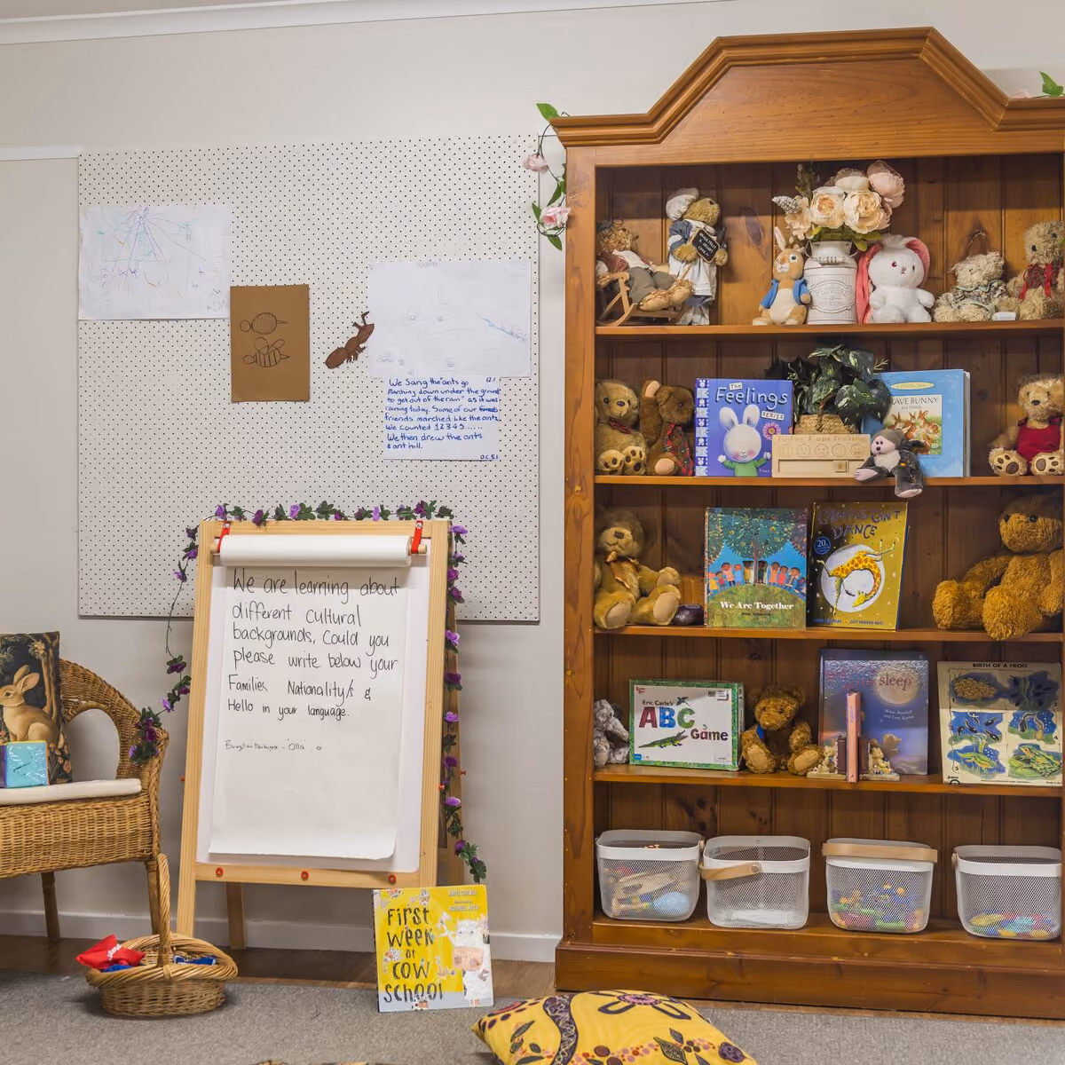 Cosy reading corner with a wooden bookcase of picture books and teddy bears, a wicker chair and an easel