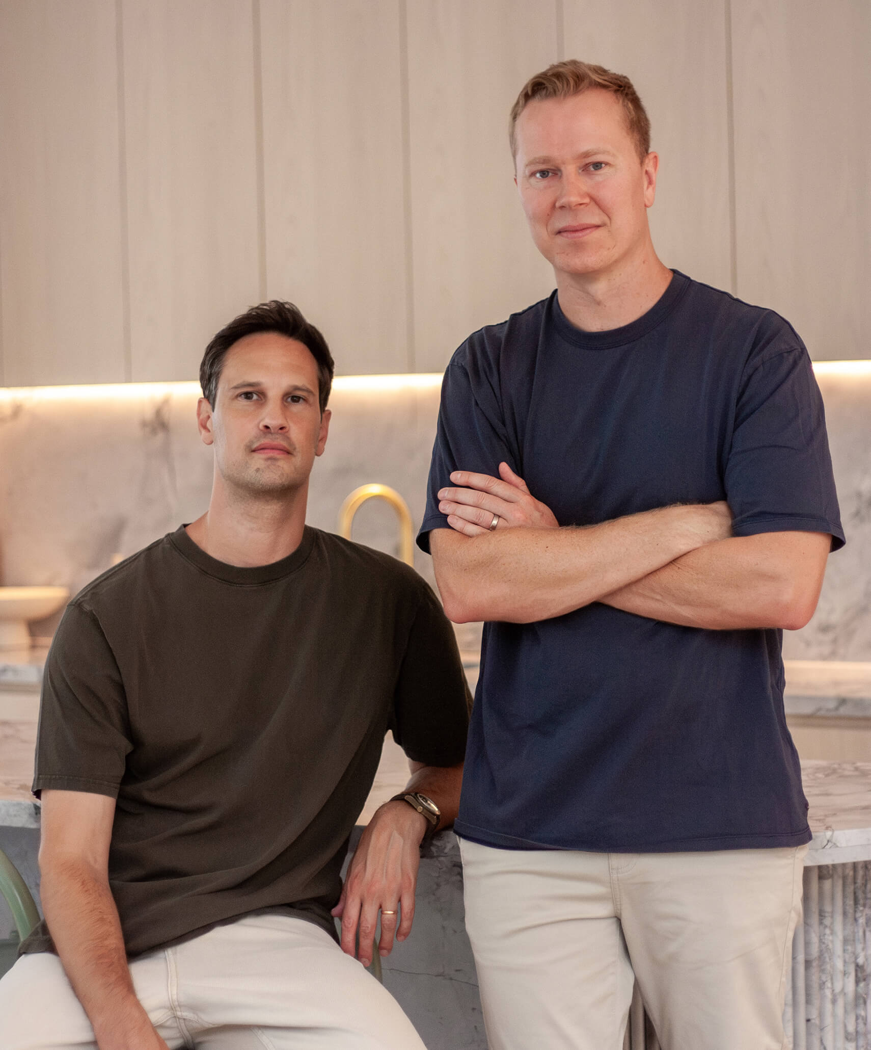 Dalcott's two founders are standing in a modern kitchen. One is sitting on a counter, while the other stands next to him with crossed arms.