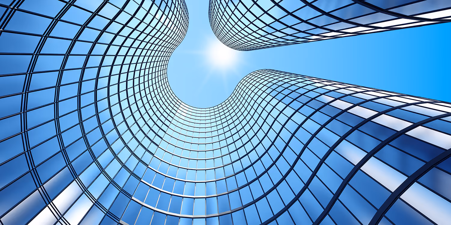 Curved glass skyscrapers with reflective blue windows against a bright blue sky with the sun.