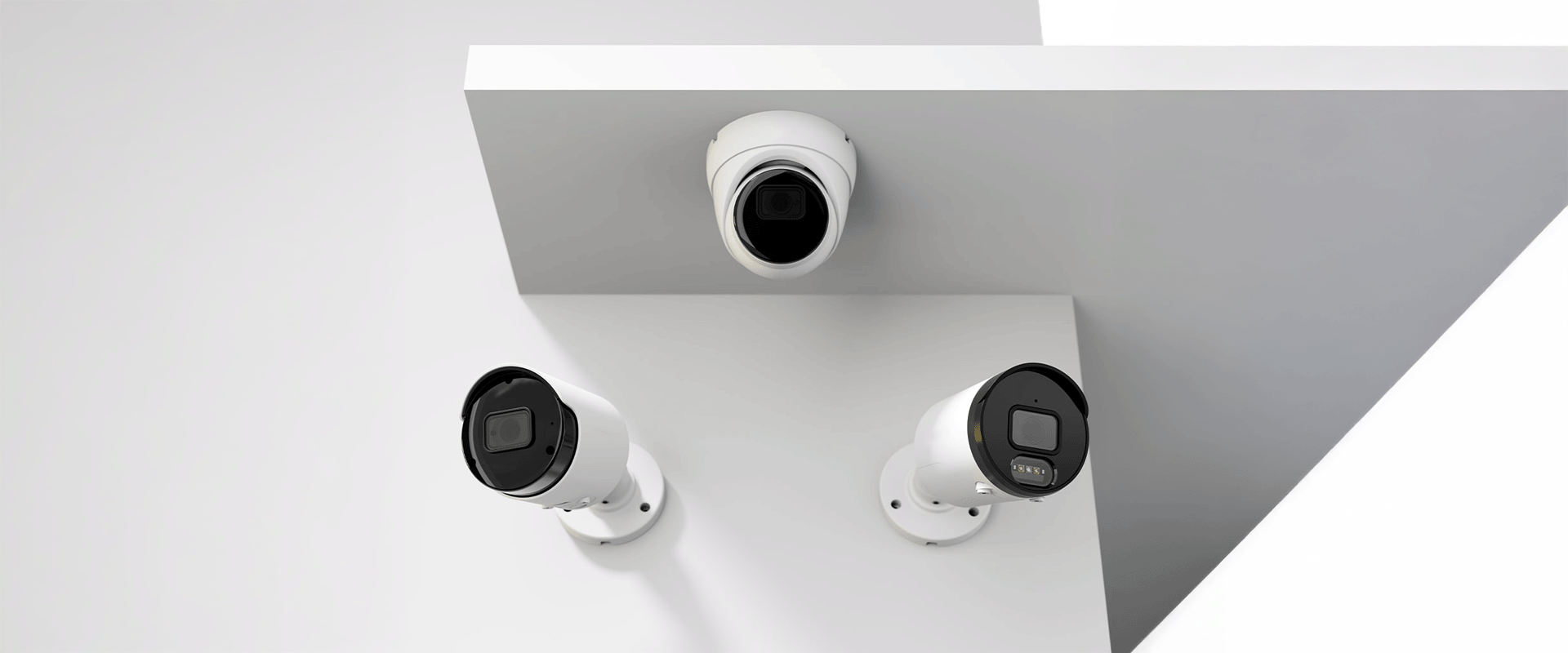 Drei Überwachungskameras, zwei mit zylindrischem Gehäuse und eine kuppelförmige, montiert an weißen Wänden.