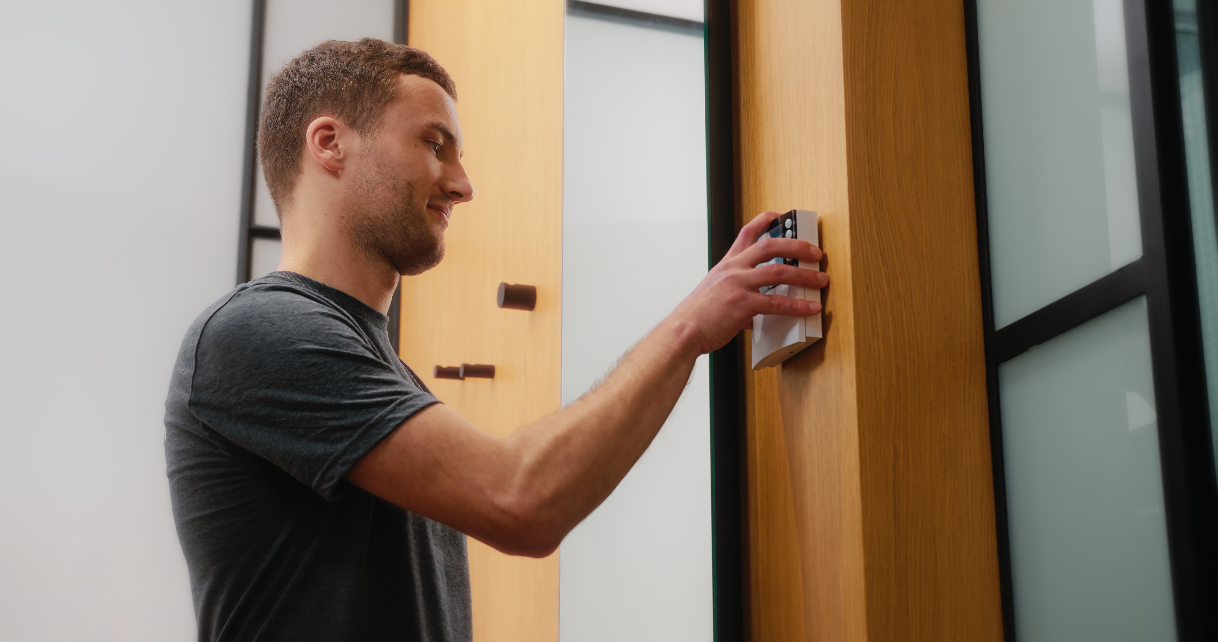 Ein Mann in einem dunkelgrauen T-Shirt bedient einen Lichtschalter oder eine Steuerung an einer Holzwand.