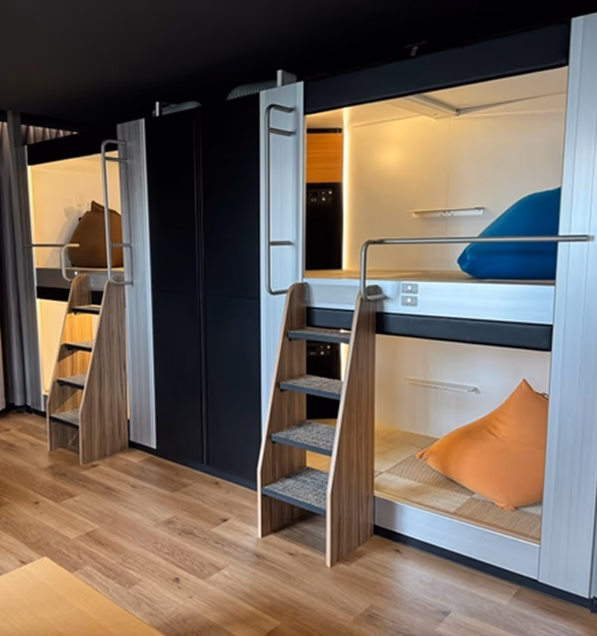 Modern interior with two sets of bunk beds, each with wooden ladders, colorful cushions, and warm ambient lighting.