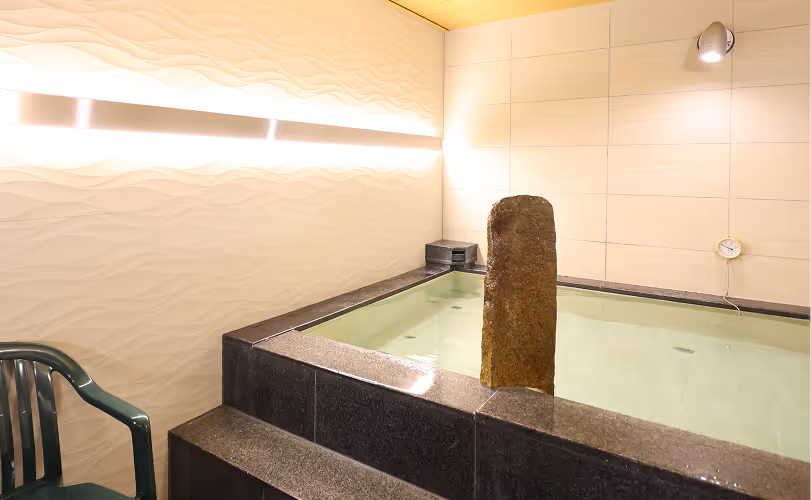 Indoor bath with stone pillars, water, step seating, and a green plastic chair.