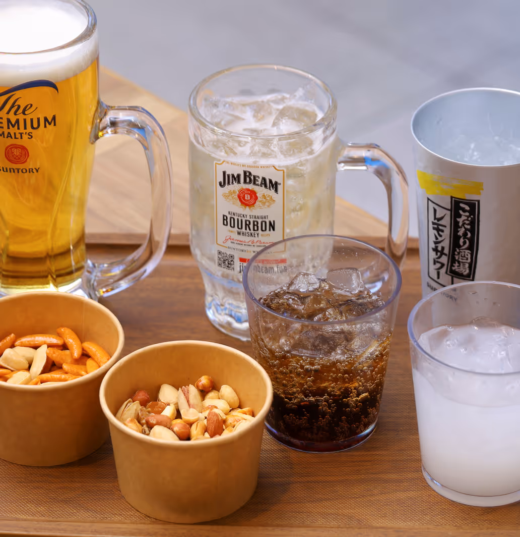 Wooden tray with assorted drinks including a beer mug, Jim Beam bourbon glass, two other glasses with ice, and two cups of mixed nuts.