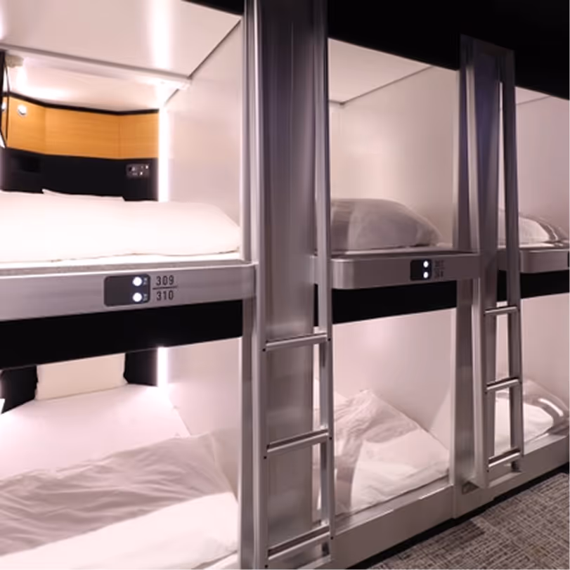 Stacked capsule-style beds with pillows and ladders in a modern sleeping pod room.