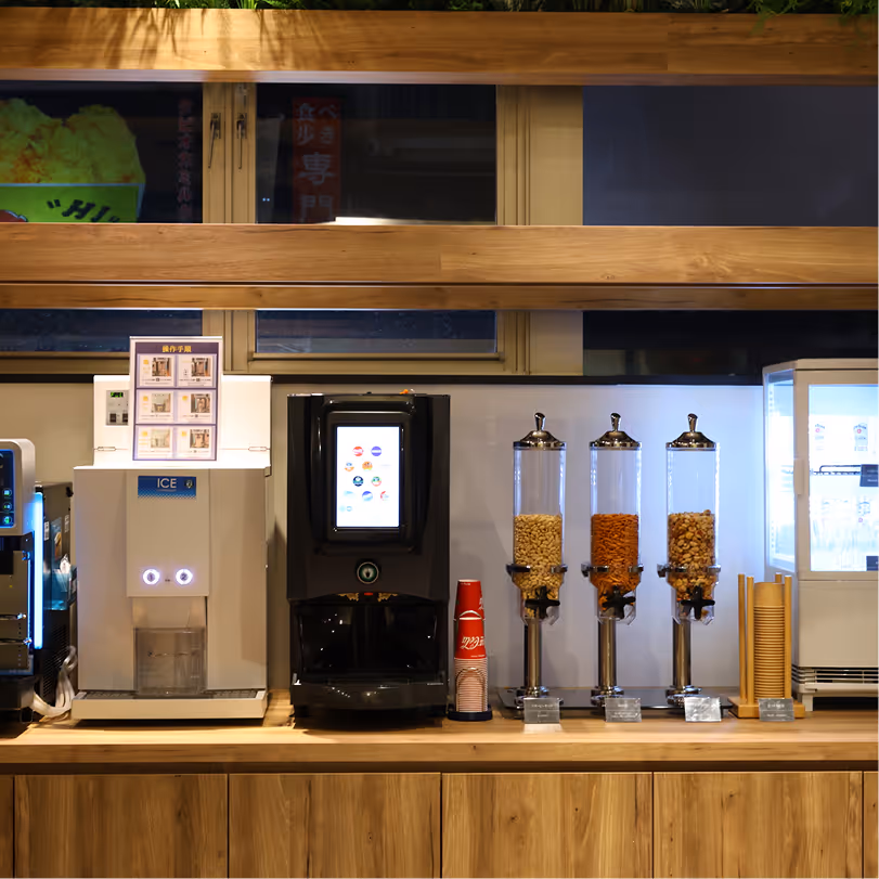 Beverage station with ice dispenser, soft drink machine, three cereal dispensers, and cups on a wooden counter.