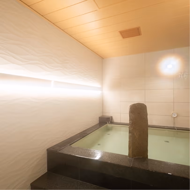 Indoor stone bath with water and soft lighting on white tiled wall and wooden ceiling.