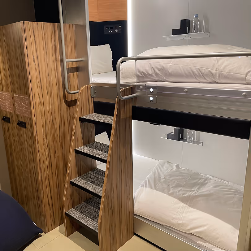 Modern wooden bunk bed with stairs, white bedding, and shelves.