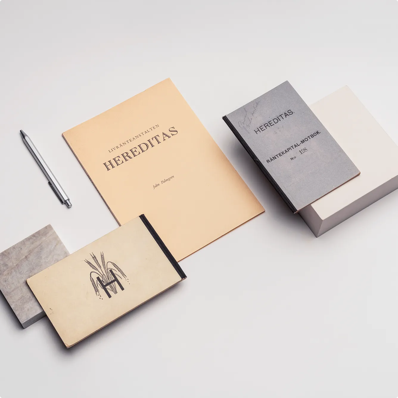 Flera vintageböcker och ett silverfärgat pennställ på ett vitt bord, med titeln HEREDITAS på två av böckerna.