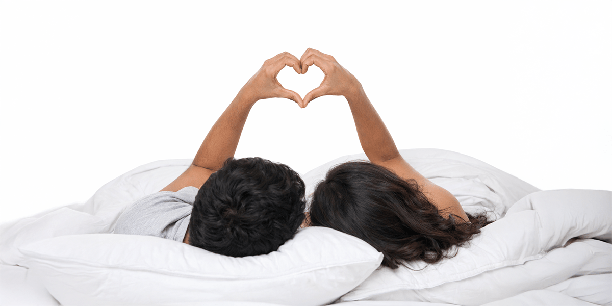 Couple relaxing in bed forming heart shape with hands representing intimacy, sexual wellness, and relationship health