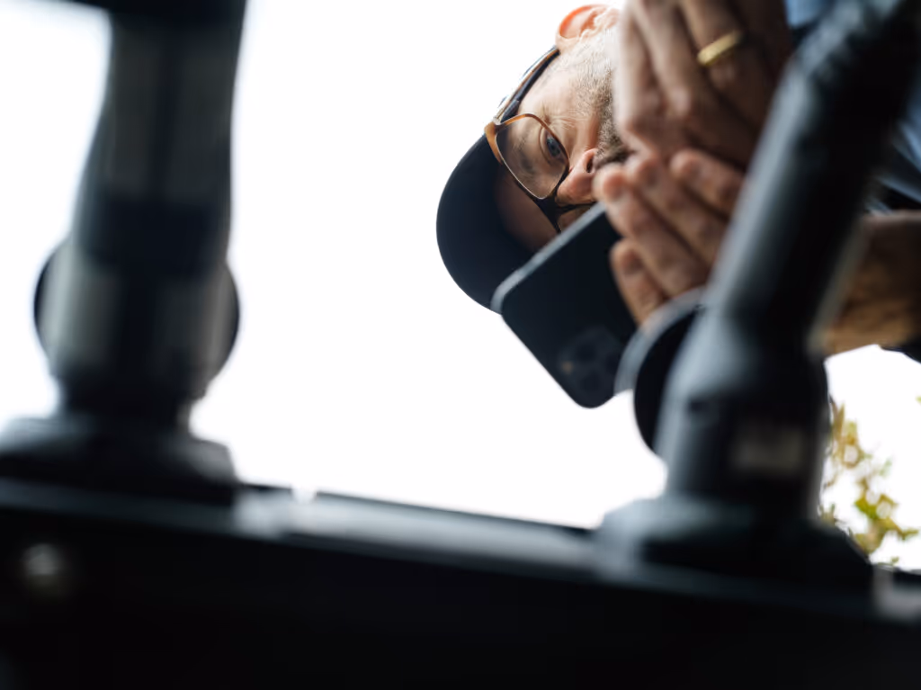 Man med keps och glasögon som håller en smartphone ovanifrån med teknisk utrustning i förgrunden.