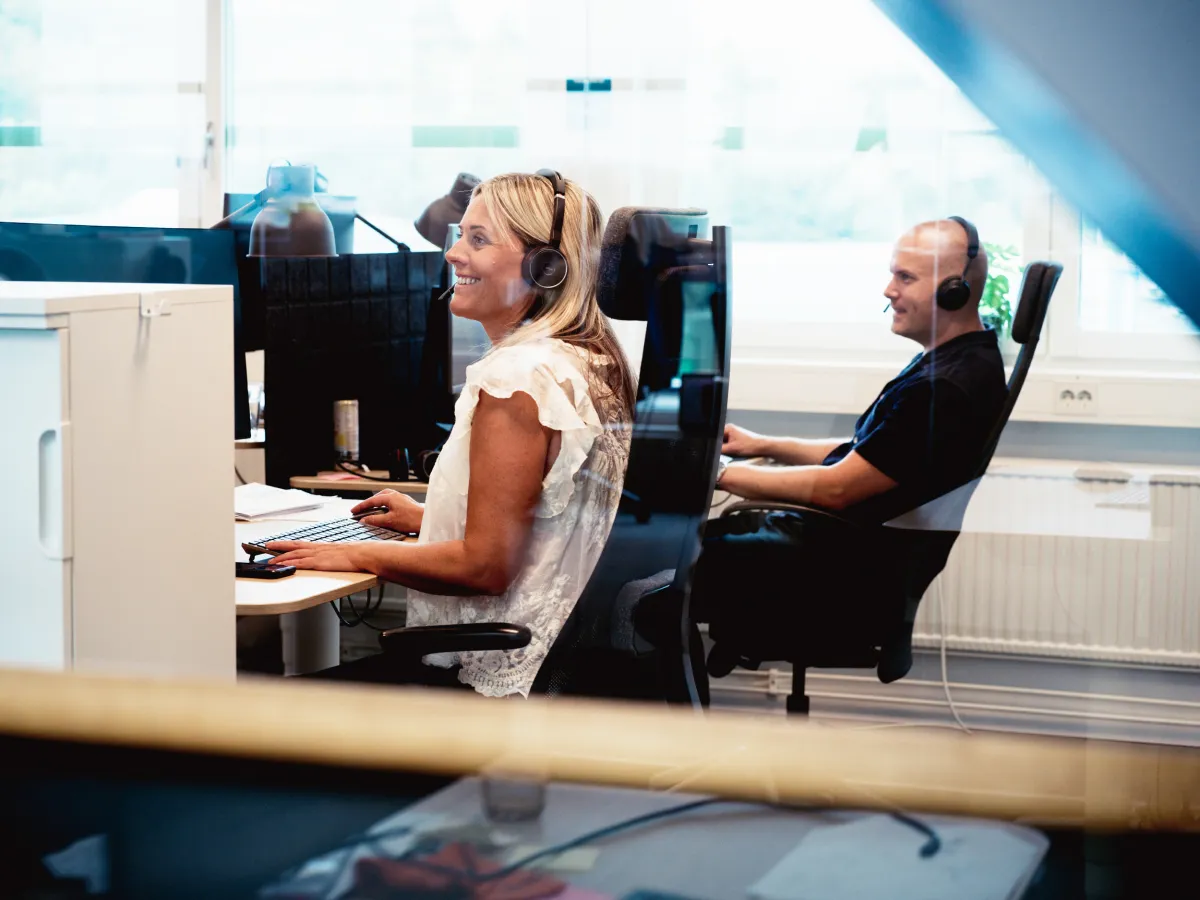 Två kundservicemedarbetare med headset arbetar vid sina datorer i ett kontorsrum.
