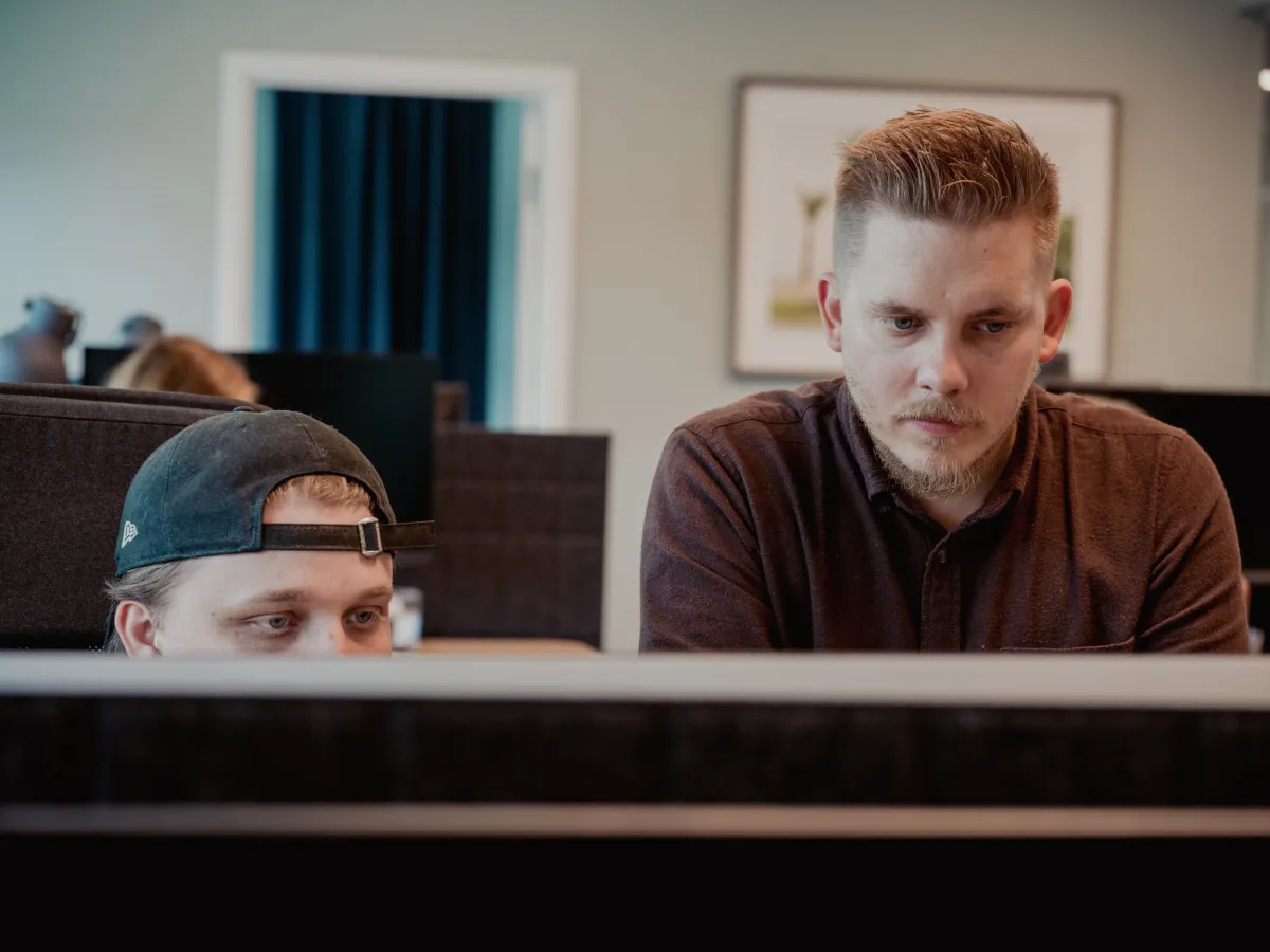 Två män som koncentrerat arbetar vid en datorskärm i ett kontorsutrymme.